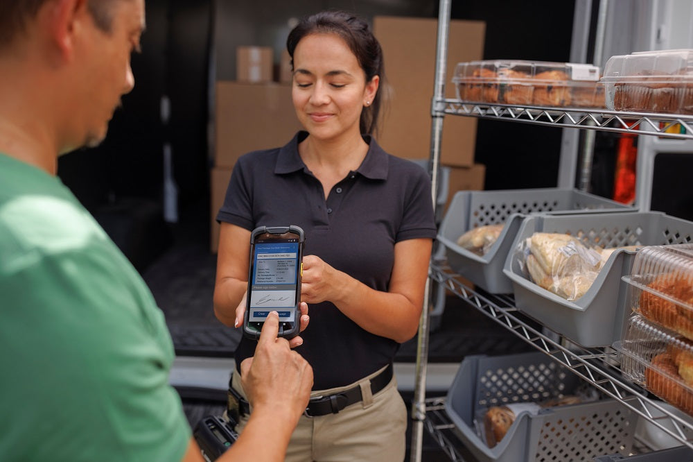 Chaufför signerar leverans på en handdator som hålls av butikspersonal.