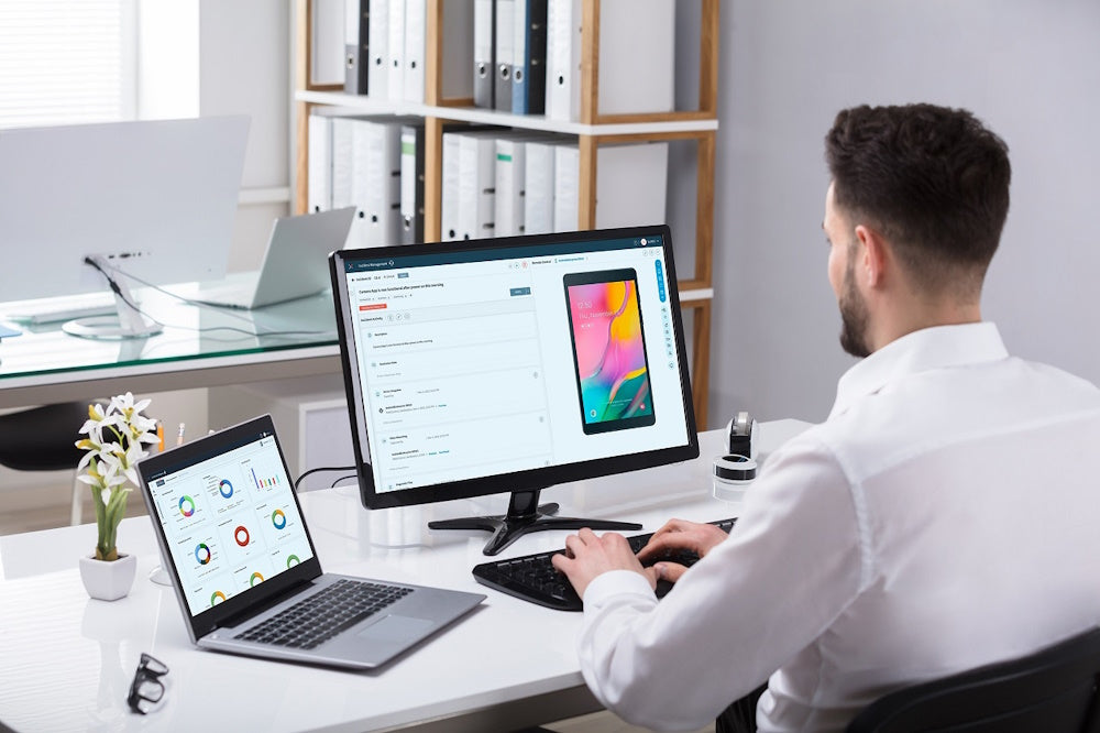 Man vid skrivbord fjärrstyr en mobil enhet via MDM-lösning på datorskärm.